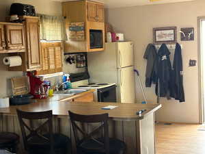 Kitchen with a kitchen breakfast bar, electric range oven, a peninsula, black microwave, and light wood-style flooring