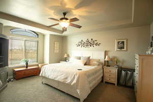 Carpeted bedroom with a raised ceiling and ceiling fan