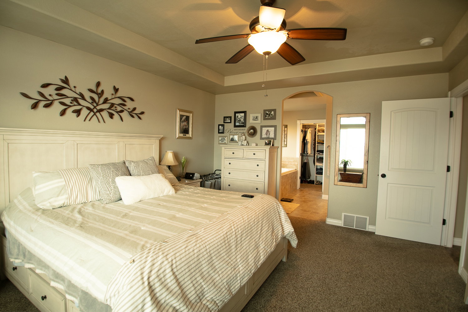 Bedroom featuring a raised ceiling, a spacious closet, dark carpet, arched walkways, and a ceiling fan