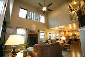 Living room featuring a ceiling fan, tiled gas fireplace, and vaulted ceiling