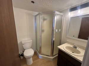 Bathroom with a stall shower, vanity, a textured ceiling, and light wood-style flooring