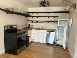 Kitchen featuring open shelves, white cabinetry, stainless steel appliances, butcher block counters, and a textured ceiling