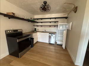 Kitchen with open shelves, stainless steel appliances, white cabinetry, light wood-type flooring, and a textured ceiling
