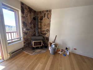 Unfurnished living room with light wood finished floors, baseboard heating, a textured ceiling, healthy amount of natural light, and a wood stove