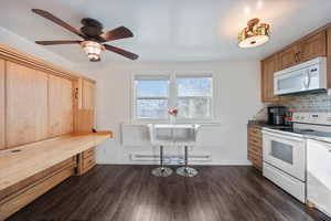 Kitchen with white appliances, dark wood-type flooring, decorative backsplash, a baseboard radiator, and ceiling fan