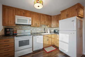 Kitchen with white appliances, dark wood-style floors, tasteful backsplash, and wood finish cabinetry