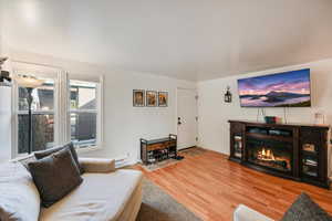 Living room featuring light wood-style flooring, a glass covered fireplace, and baseboard heating