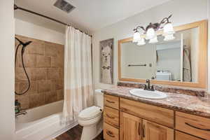 Bathroom with vanity, washer / clothes dryer, shower / bathtub combination with curtain, and dark wood-type flooring