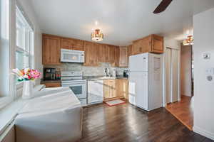 Kitchen featuring white appliances, dark wood-style floors, ceiling fan, wood finish cabinetry, and light countertops