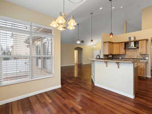 Kitchen featuring arched walkways, a breakfast bar, light stone counters, a chandelier, and dark wood-style flooring