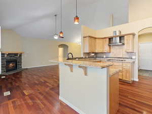 Kitchen featuring arched walkways, a peninsula, light wood finish cabinets, a breakfast bar area, and light stone countertops