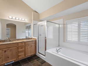 Full bath with double vanity, a shower stall, lofted ceiling, a garden tub, and dark stone finish flooring