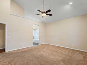 Carpeted spare room with ceiling fan, vaulted ceiling, and arched walkways
