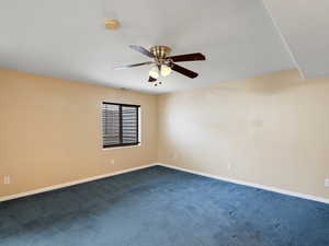 Empty room with a ceiling fan, dark carpet, and a smoke detector