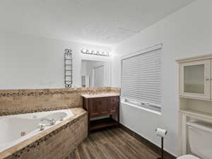 Bathroom with vanity, a tub with jets, wood finish floors, and a textured ceiling