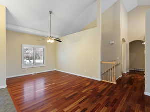 Spare room featuring vaulted ceiling, arched walkways, dark wood-type flooring, and a ceiling fan