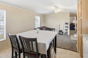 Dining space with a ceiling fan, ornamental molding, lofted ceiling, and light carpet