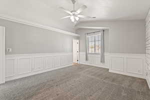 Carpeted empty room with ceiling fan, a wainscoted wall, and a decorative wall