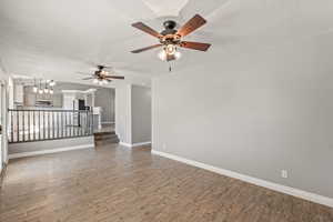 Empty room featuring a textured ceiling, light wood finished floors, a ceiling fan, and suspended lighting