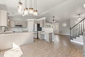 Kitchen with a peninsula, tasteful backsplash, a ceiling fan, white appliances, and decorative light fixtures