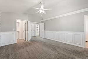 Unfurnished bedroom featuring a decorative wall, wainscoting, carpet flooring, a ceiling fan, and a spacious closet