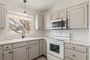 Kitchen featuring electric range, stainless steel microwave, light stone counters, and backsplash