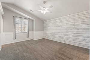 Empty room with a wainscoted wall, a ceiling fan, carpet flooring, and a decorative wall