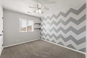 Spare room featuring ceiling fan, dark colored carpet, and a textured ceiling