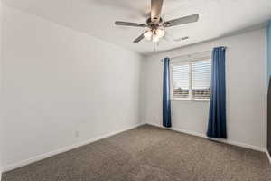 Spare room featuring dark carpet, a ceiling fan, and a textured ceiling