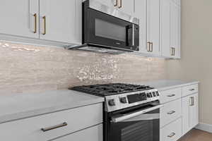 Kitchen featuring stainless steel appliances, white cabinets, light stone countertops, and backsplash