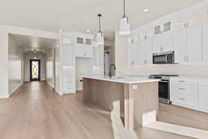 Kitchen with decorative backsplash, glass insert cabinets, stainless steel appliances, dual tone cabinetry, and a center island with sink