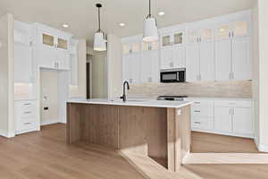 Two tone kitchen featuring glass insert cabinets, a kitchen island with sink, decorative backsplash, dual tone cabinets, and pendant lighting