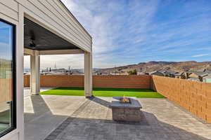Fenced backyard featuring an outdoor fire pit, a patio area, ceiling fan, a residential view, and a mountain view