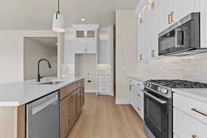 Kitchen with two tone cabinetry, stainless steel appliances, glass insert cabinets, light stone counters, and light wood finished floors