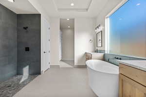 Bathroom featuring vanity, a soaking tub, a walk in shower, recessed lighting, and a tray ceiling