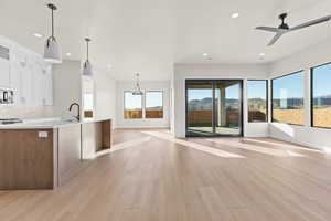 Kitchen with glass insert cabinets, ceiling fan, open floor plan, light wood-style floors, and light stone counters