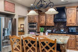 Kitchen with stainless steel appliances, dark stone counters, decorative backsplash, and a kitchen bar