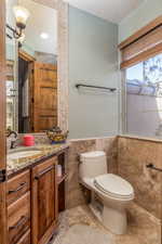 Half bathroom featuring vanity, plenty of natural light, wainscoting, and tile walls