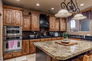 Kitchen with double oven, dark stone countertops, a kitchen island, backsplash, and wood finish cabinetry