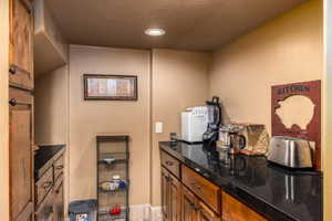 Bar area with wood finish cabinets, recessed lighting, and dark stone countertops