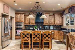 Kitchen featuring stainless steel appliances, wood finish cabinets, exhaust hood, a center island, and decorative backsplash