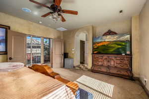 Bedroom featuring access to exterior, light colored carpet, arched walkways, and a ceiling fan