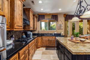 Kitchen with a kitchen island, dark stone countertops, hanging light fixtures, black gas cooktop, and tasteful backsplash