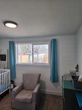 Bedroom featuring a nursery area, dark colored carpet, multiple windows, and wood walls