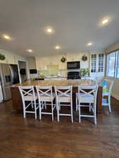 Dual tone kitchen with black appliances, dark wood-type flooring, a spacious island, dual tone cabinetry, and a breakfast bar area