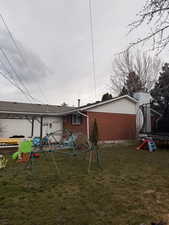 Back of house with a trampoline, a lawn, a playground, and brick siding