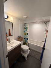 Bathroom with vanity, a textured ceiling, shower / tub combo with curtain, and dark tile patterned flooring