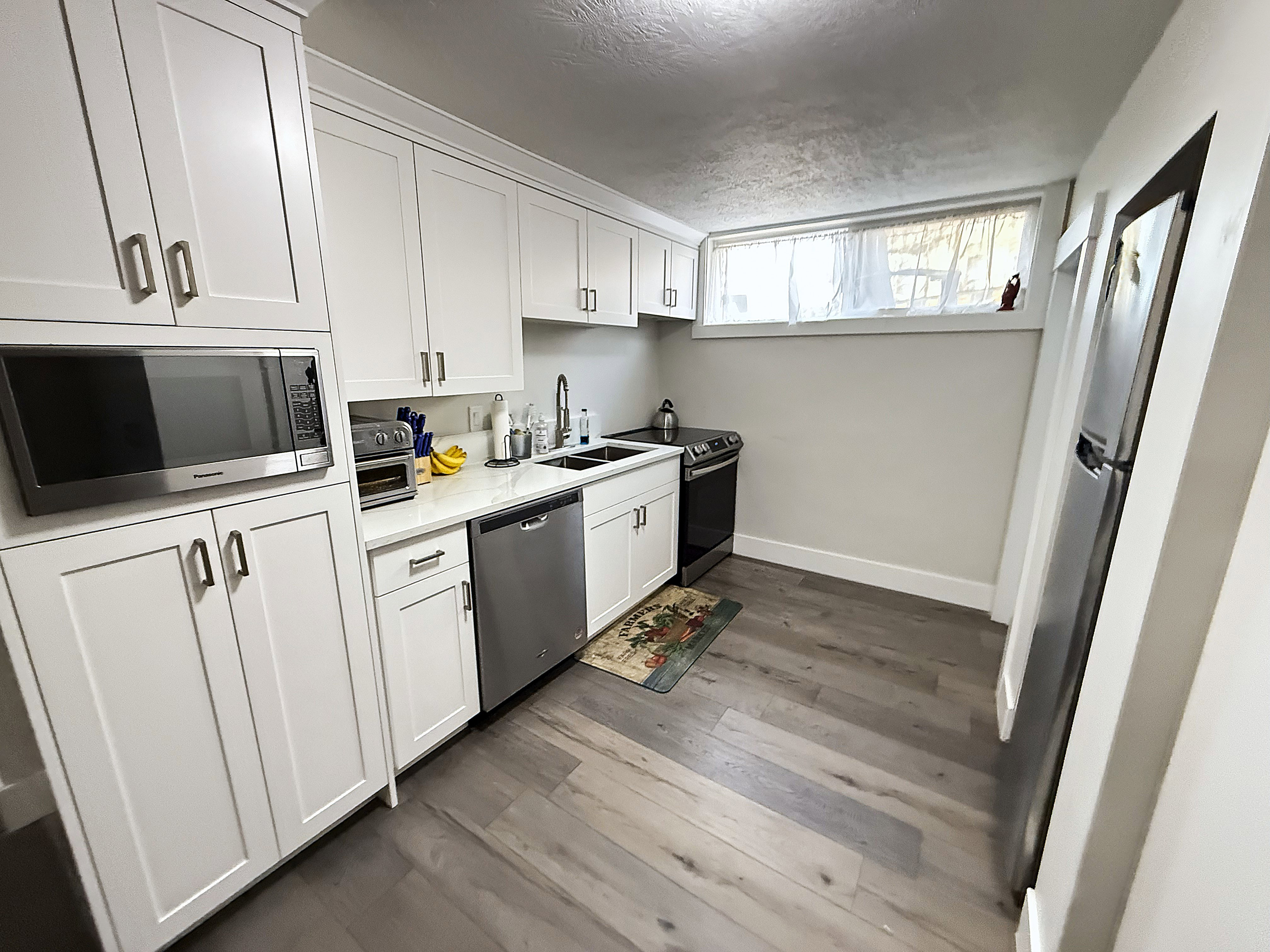 Kitchen featuring stainless steel appliances, white cabinetry, a textured ceiling, dark wood finished floors, and light stone counters