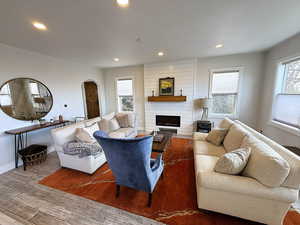 Living room featuring arched walkways, recessed lighting, wood-type flooring, and a large fireplace