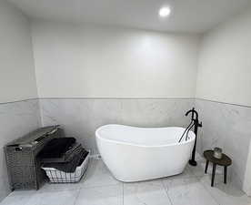 Bathroom with wainscoting, tile walls, a freestanding bath, light marble finish floors, and recessed lighting